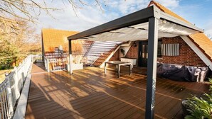 Une terrasse extérieure couverte, avec une table et des chaises, un mur en briques et une structure de toit en bois.