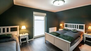 Une chambre à coucher avec un lit blanc, deux tables de chevet avec des lampes, une fenêtre et un luminaire au plafond.