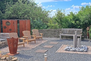 An outdoor seating area with wooden chairs and a bench, surrounded by a gravel path and decorative elements. - Holiday apartment Klever Berg (Kleve)