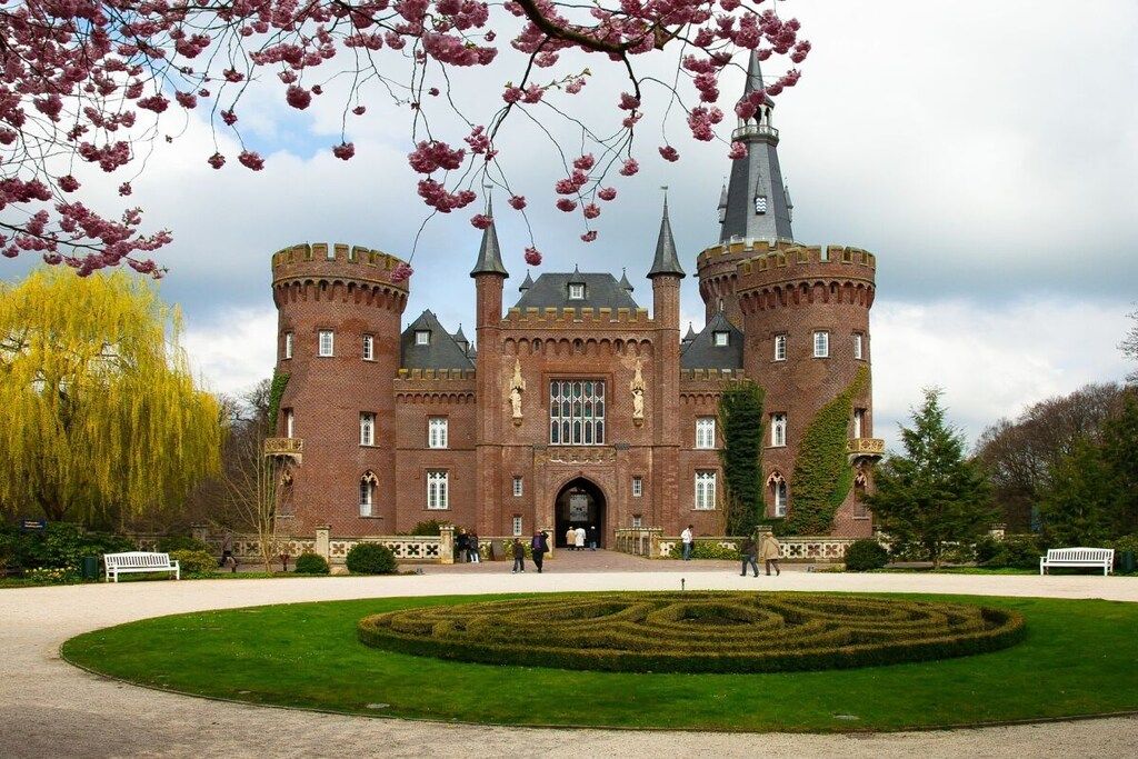 Un château historique doté d’une cour centrale, entouré de jardins soignés et d’un grand arbre.