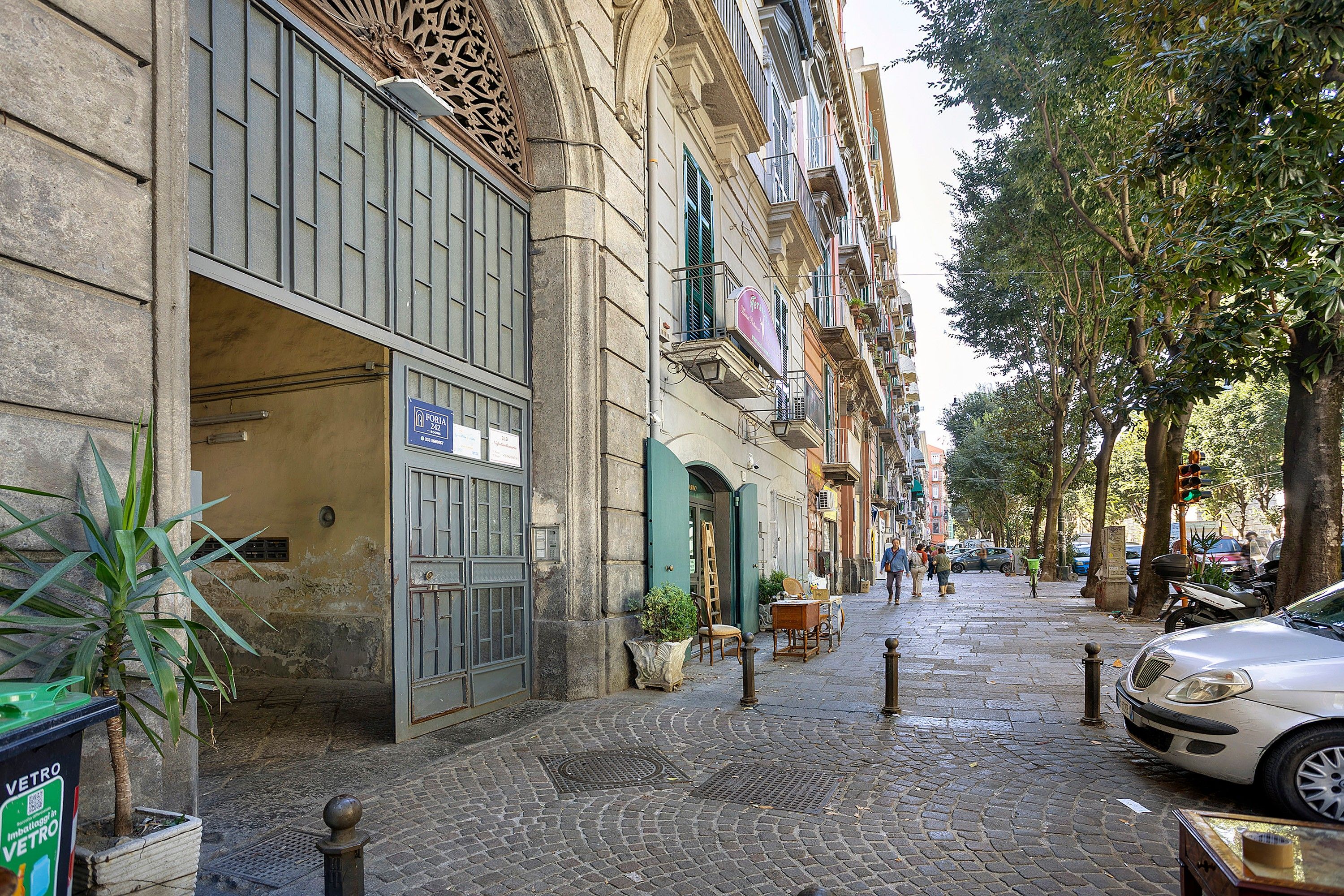 Una calle adoquinada con edificios, un coche aparcado y algunos peatones.
