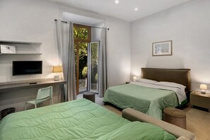 Ein Hotelzimmer mit zwei Betten, einem Schreibtisch mit Computer, einem Stuhl und einem kleinen Tisch mit Lampe.