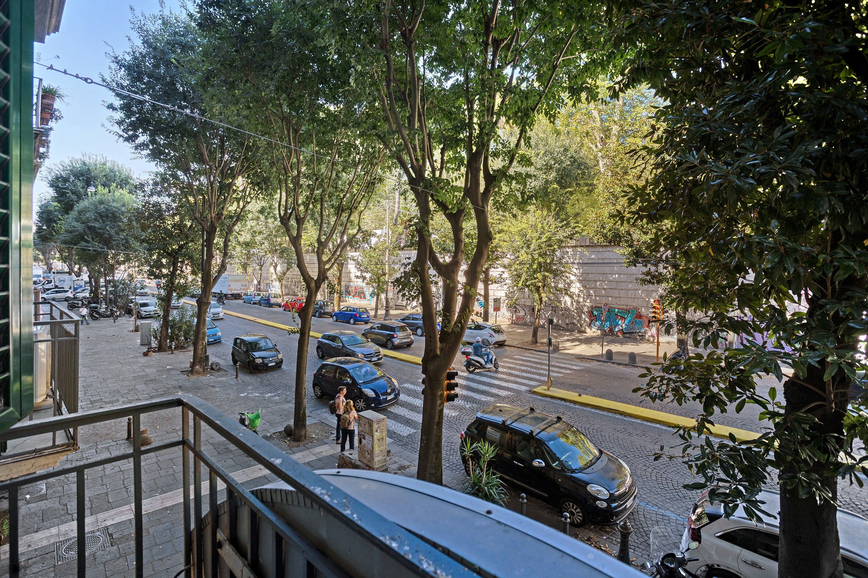Een straatbeeld met geparkeerde auto's, bomen langs de weg en een voetgangersoversteek.
