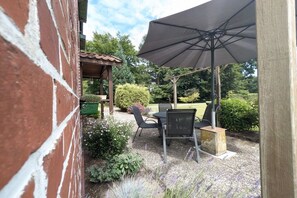 An outdoor patio with a table and chairs, an umbrella, and a brick wall. - Holiday farmhouse with 2 bedrooms (Schneverdingen)