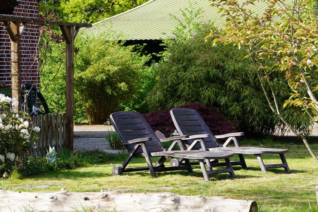 Un giardino con due poltrone e un tavolo, immerso nel verde e adiacente a un edificio in mattoni.