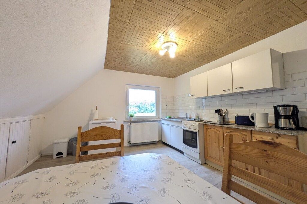Une cuisine avec des meubles blancs, un plafond en bois et une fenêtre qui laisse entrer la lumière naturelle.