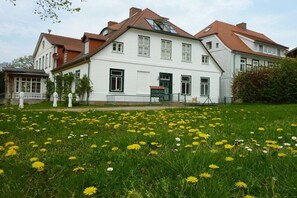 Un edificio grande y blanco con muchas ventanas y techo rojo, rodeado por un campo lleno de flores amarillas y blancas.