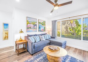 Ein Wohnzimmer mit Ecksofa, Couchtisch, Beistelltisch mit Lampe und Kunstwerken an den Wänden.