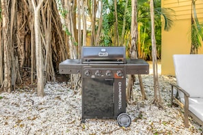 An outdoor grill with a control panel, surrounded by gravel and palm trees. - Gertrude's Siesta | 100% Private, 2-min to Beach Path! Dining & Music! Snorkeling, Sunsets! (Siesta Key)