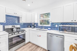 Une cuisine moderne avec des armoires blanches, une cuisinière en acier inoxydable, un lave-vaisselle et un dosseret de carrelage bleu.