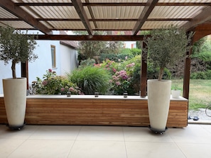 A covered outdoor seating area with a wooden bench and two large planters.