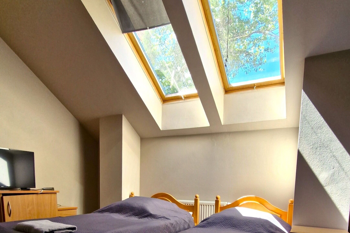 Quarto com cama, escrivaninha e dois claraboias.