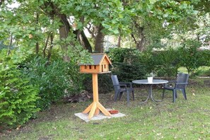 A wooden birdhouse on a stand, a round table with two chairs, and a small bowl on the ground. - Holiday home in Aurich with swimming pool (Aurich)