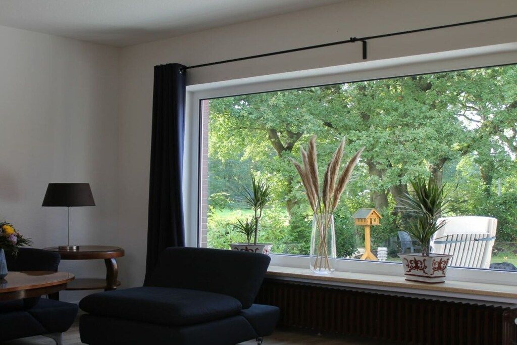A room with a large window, a dark sofa, a small table with a lamp, and decorative items on the windowsill.
