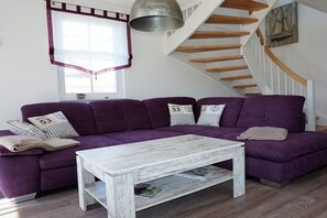Ein Wohnzimmer mit einem violetten Ecksofa, einem weißen Couchtisch und einer Treppe mit Holzbalken.