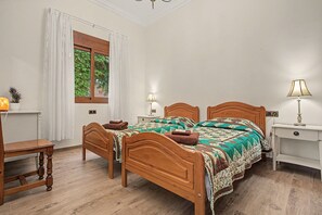 A bedroom with a wooden bed, two bedside tables, a nightstand, a lamp, a window with curtains, and a small plant. - Villa Samarin – Golf & Ocean View (Adeje)