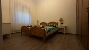 A bedroom with two wooden beds, a nightstand with a lamp, a wardrobe, and a window with curtains. - Villa Samarin – Golf & Ocean View (Adeje)