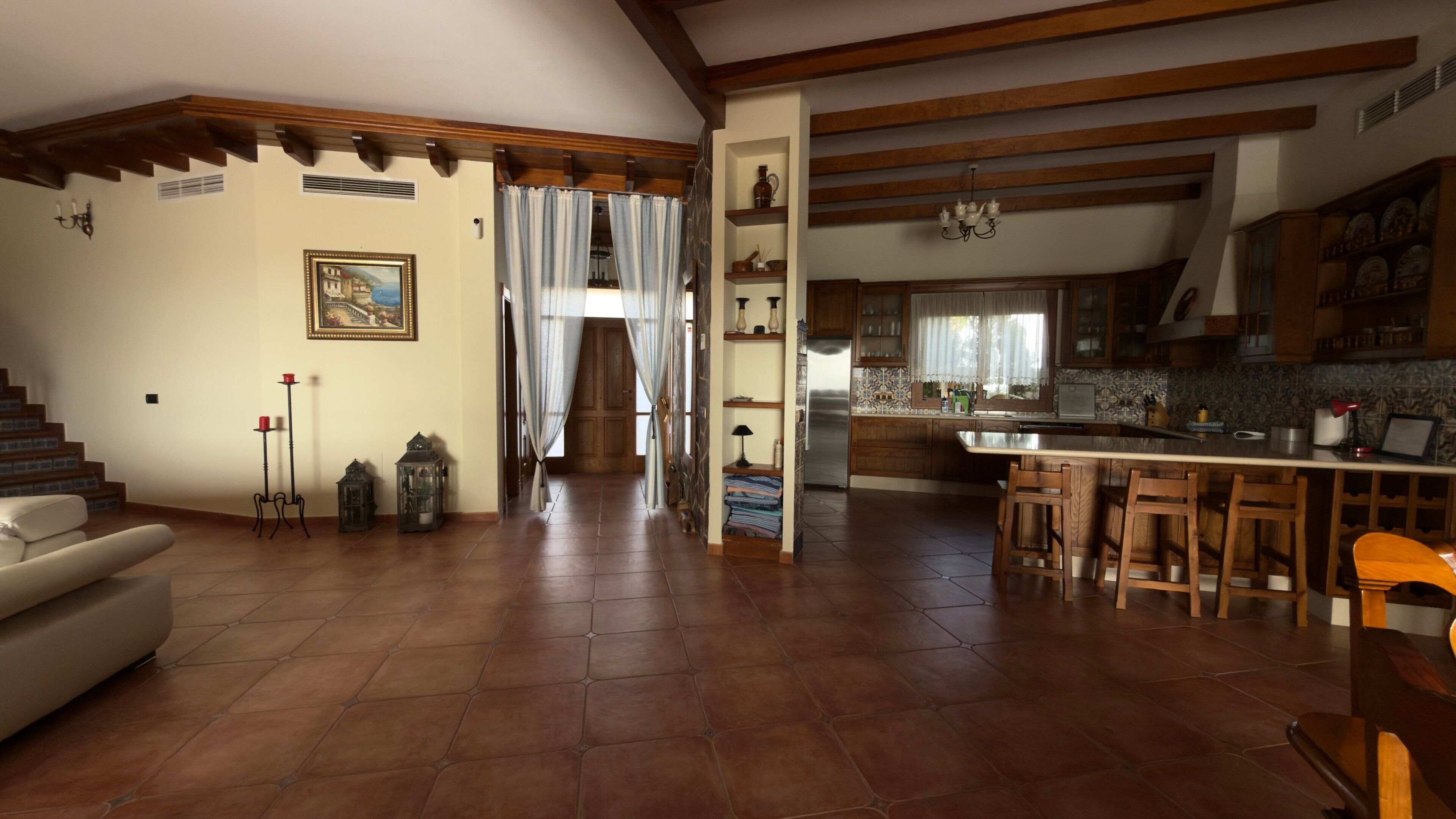 Amplia sala de estar con escalera, cocina con barra y comedor con sillas de madera.