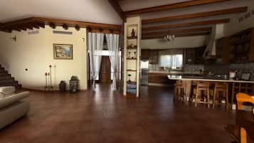 Amplia sala de estar con escalera, cocina con barra y comedor con sillas de madera.