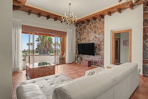 A spacious living room with a stone accent wall, a flat-screen TV, a white leather sofa, and a wooden ceiling.