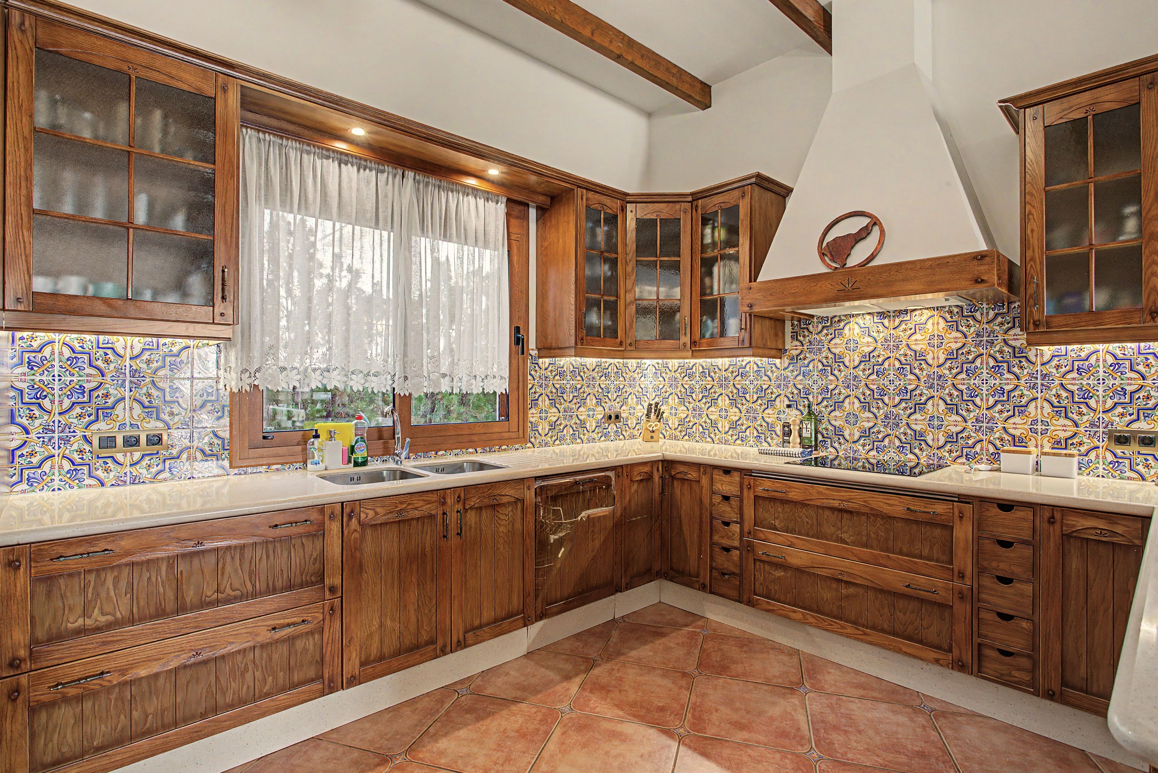 A kitchen with wooden cabinets, a tiled backsplash, and a window with curtains.