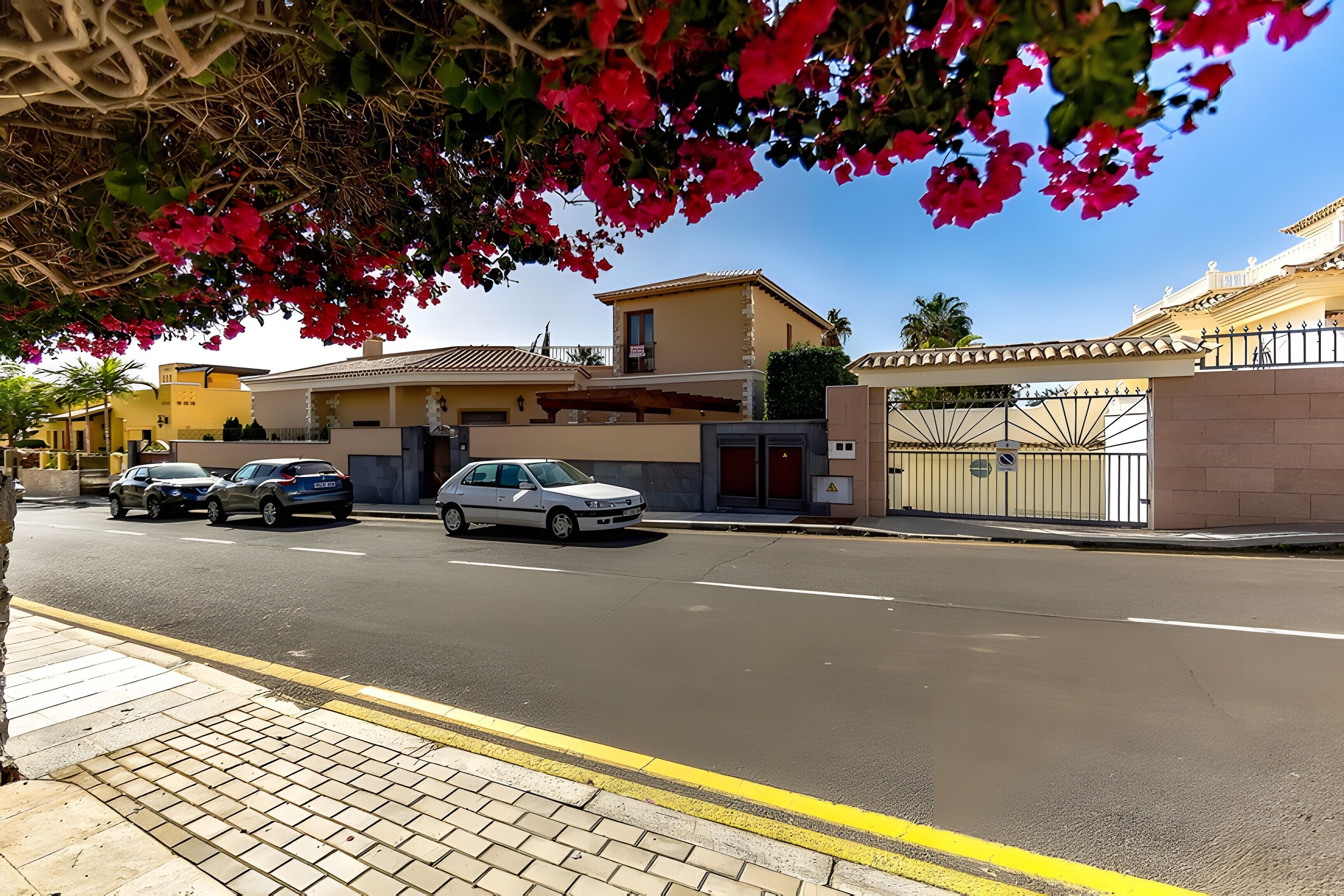 Vista de la calle con un edificio de techo plano, entrada con portón y puerta de garaje visible.