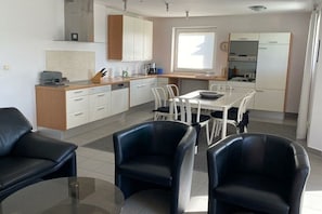 A modern kitchen with white cabinets, a dining area with a glass table, and black chairs. - Holiday apartment with terrace (RYN)