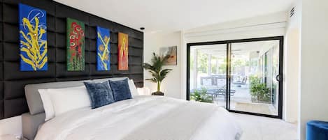 Un dormitorio moderno con una cama grande, cabecera negra y puerta de cristal corredera que da a un balcón.