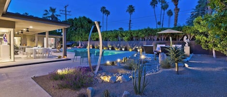 A modern outdoor pool area with a covered seating area and a well-maintained garden.
