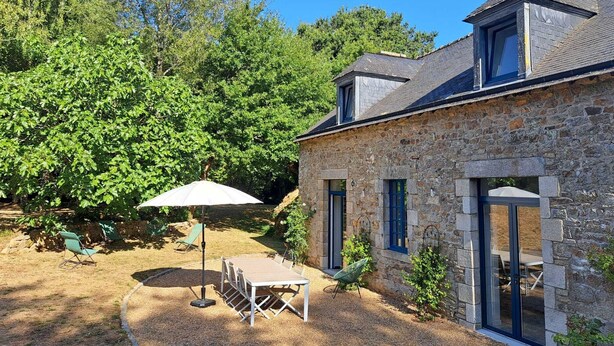 Een stenen huis met een terras, tuinmeubilair en een grote parasol.