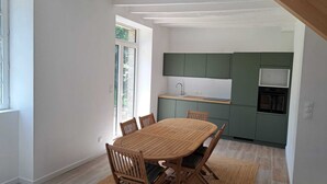 Een moderne keuken met groene kastjes, een ingebouwde oven en een eethoek met een houten tafel en stoelen.