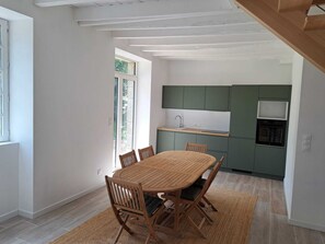 A modern kitchen with green cabinets, a built-in oven, and a dining area with a wooden table and chairs. - Vrbo Property (Le Guerno)