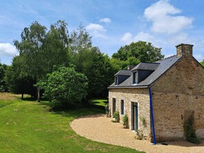 A stone building with a sloped roof, surrounded by a grassy area and trees. - Vrbo Property (Le Guerno)