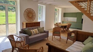 Een ruime woonkamer met een bank, stoelen, een eettafel en een keuken op de achtergrond.