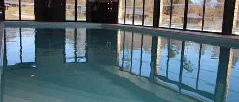Una piscina interior con paredes de vidrio transparente, piso de baldosas y vistas al exterior a través de amplias ventanas.