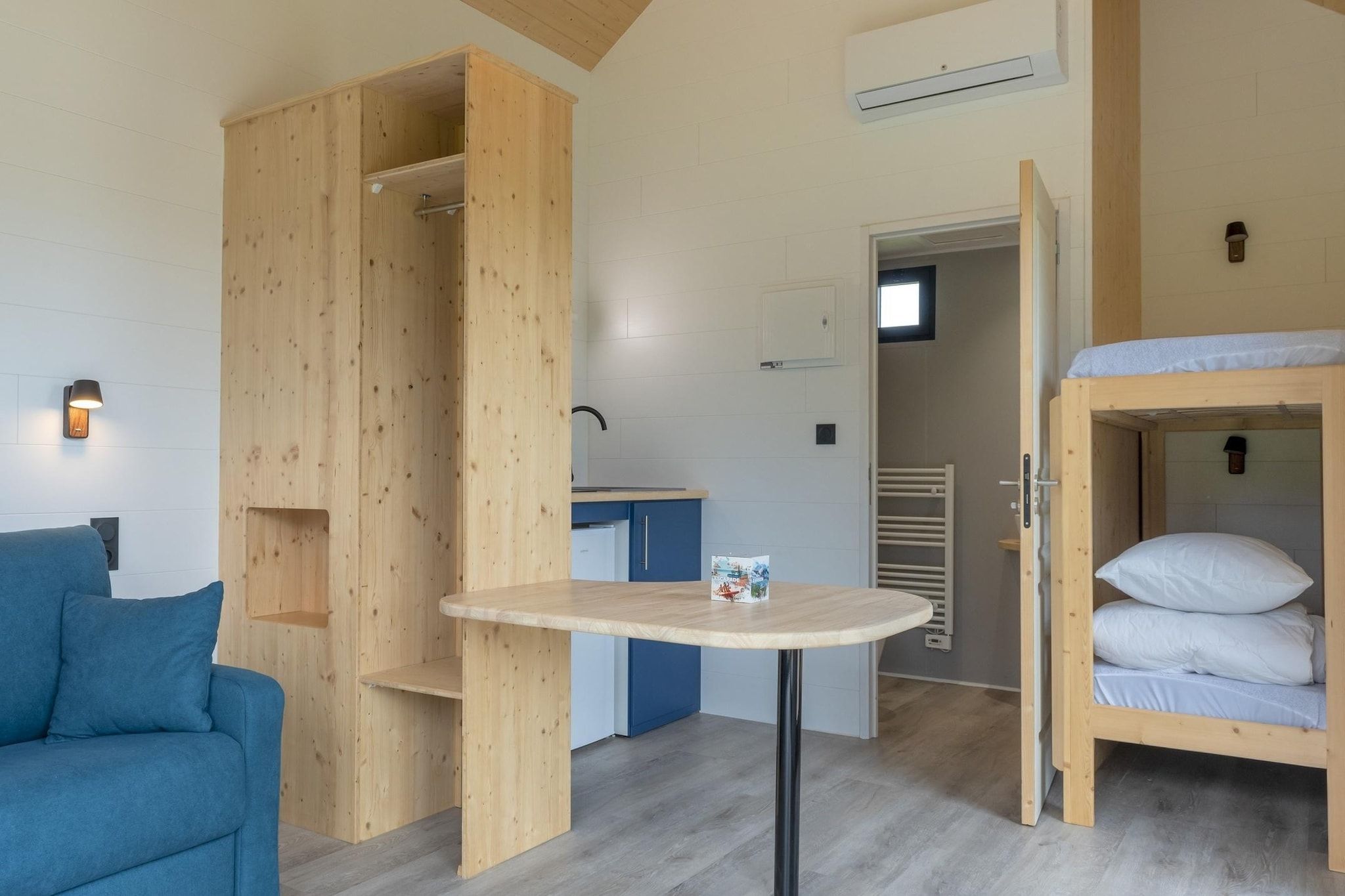 A compact room with a bunk bed, a small table, a sofa, and a kitchenette.