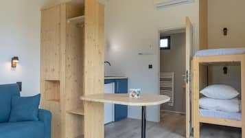 A compact room with a bunk bed, a small table, a sofa, and a kitchenette.