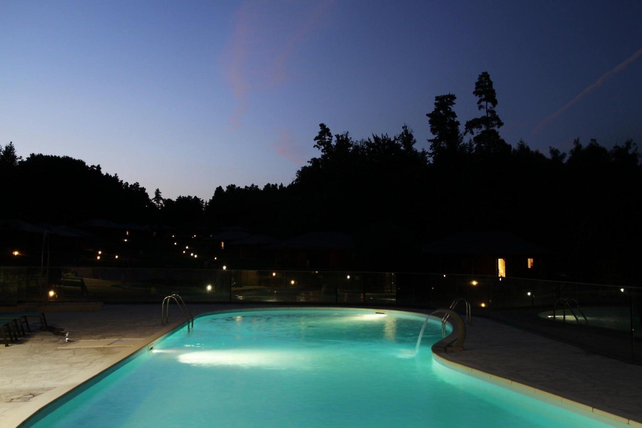 Piscina ao entardecer com árvores e cerca ao redor.