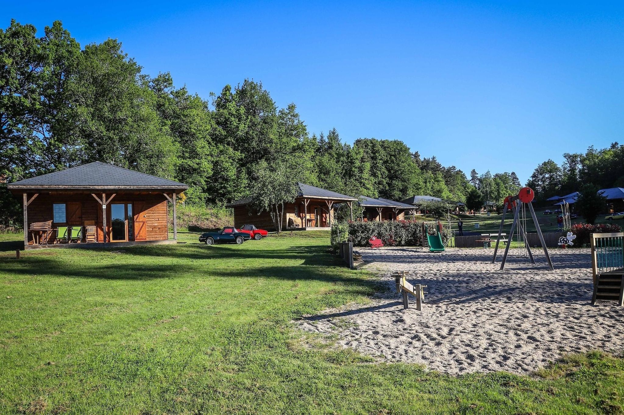 Un terrain de camping doté de cabanes en bois, d’une aire de jeux et d’un ciel d’un bleu limpide.