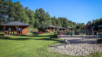 Un terrain de camping doté de cabanes en bois, d’une aire de jeux et d’un ciel d’un bleu limpide.