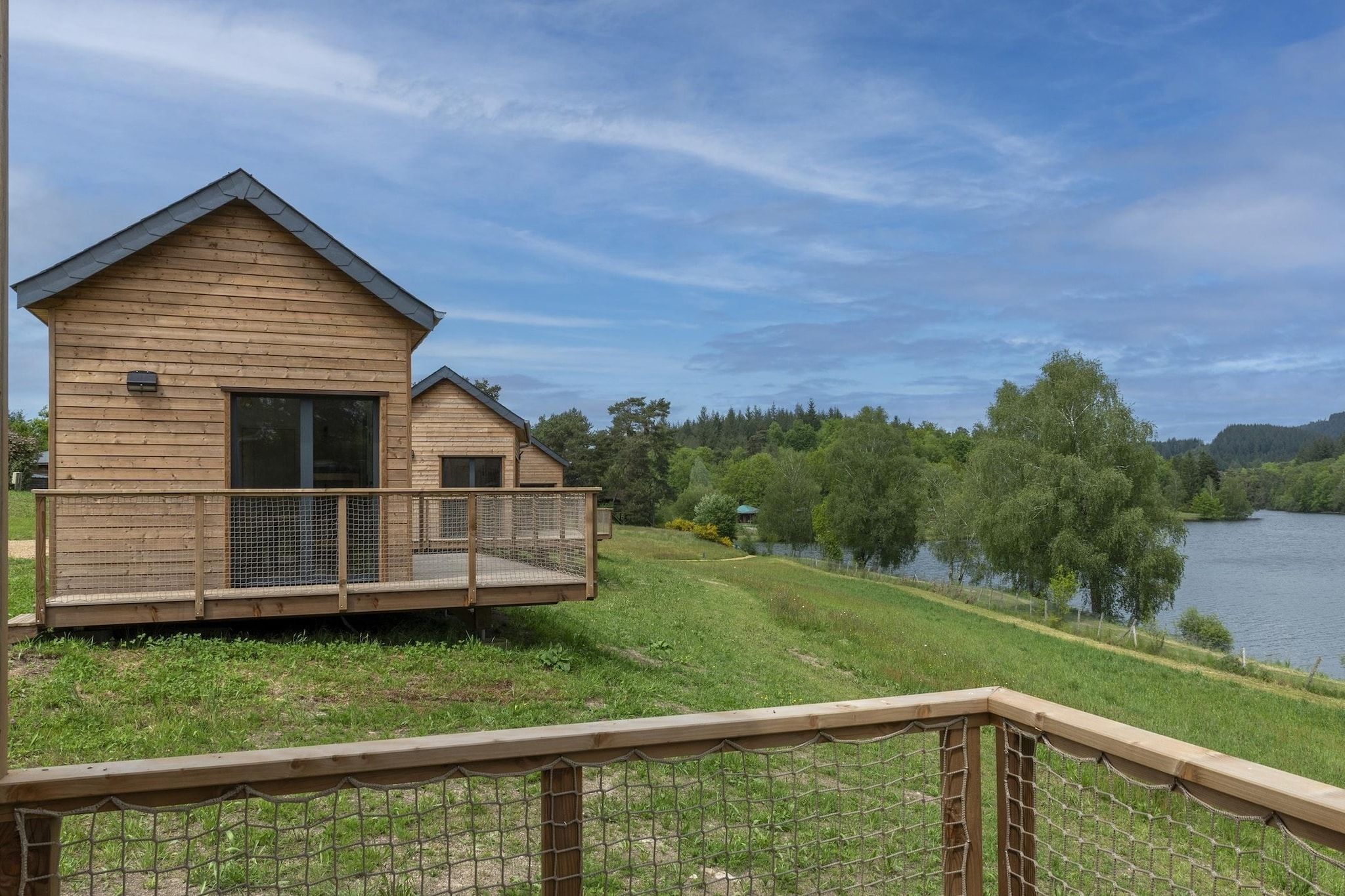 A wooden cabin with a balcony overlooking a lake, surrounded by trees.