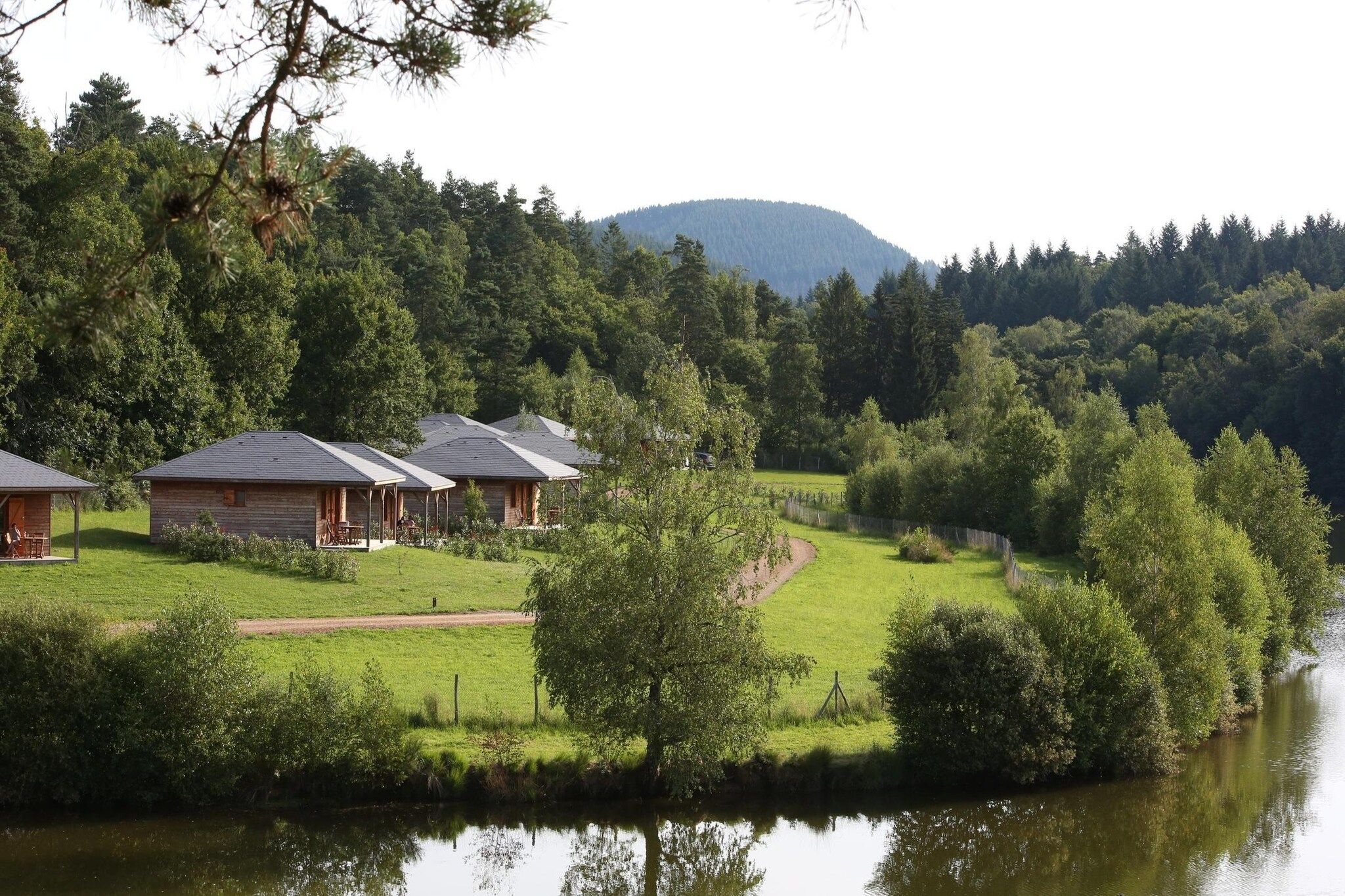 Uma propriedade à beira do lago com cabanas, uma área gramada e uma colina arborizada ao fundo.