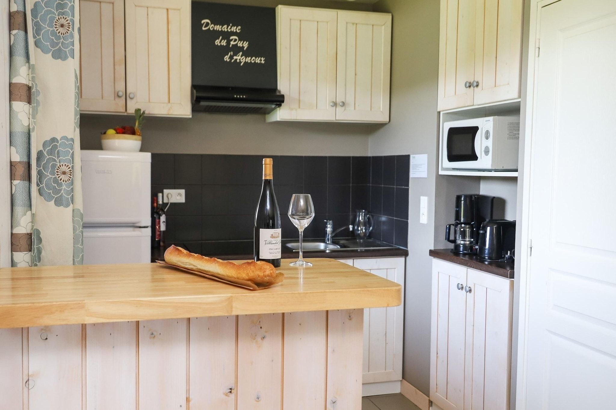 A kitchen with a wooden countertop, a bottle of wine, a wine glass, and a loaf of bread.