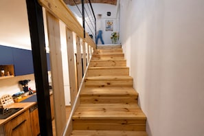A wooden staircase in a room with a kitchen area on the left.