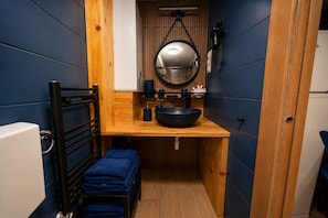 A compact bathroom with a wooden vanity, a large mirror, and a black sink.