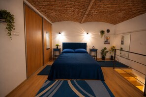 A bedroom with a bed, bedside tables, a nightstand, a potted plant, a wall clock, and a ceiling with exposed brick. - Cozy 1-bedroom apartment in Budapest (Budapest)