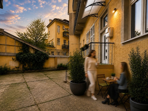 A courtyard with a building featuring balconies, a large potted plant, and a table with chairs.