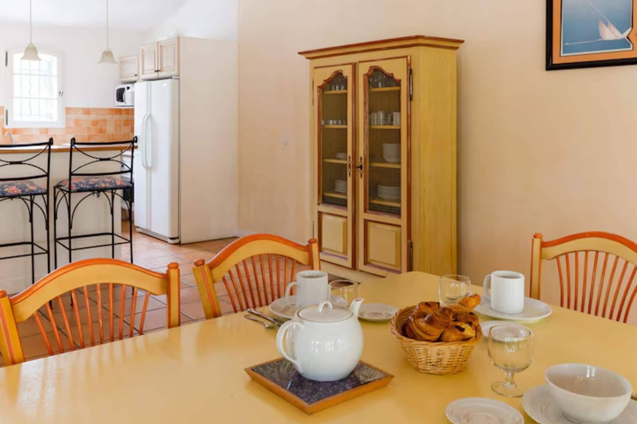 A dining area with a table set for two, a cabinet with glass doors, and a kitchen in the background.