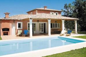 Una casa de dues plantes amb piscina, mobiliari exterior i una pèrgola.