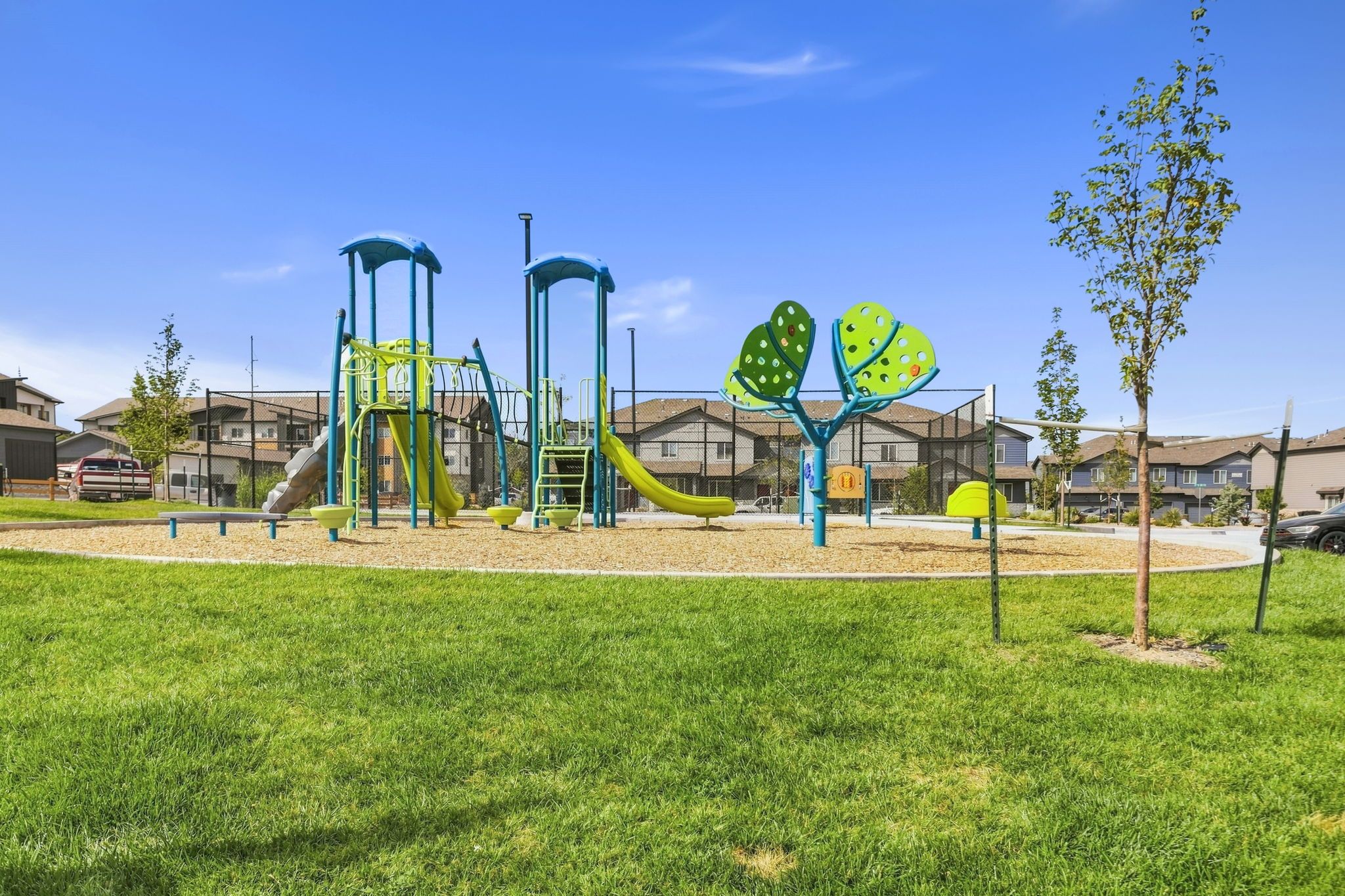 Un parque infantil con toboganes y estructuras para escalar, rodeado de césped y edificios residenciales.